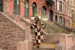 black with with long braids wearing a black and brown boucle coat and standing in front of a stoop in brooklyn